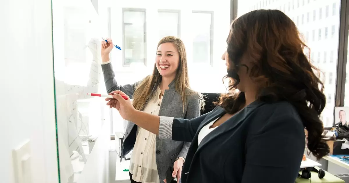 a woman pointing at a whiteboard with a pen