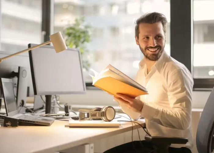 a man sitting at a desk holding a book