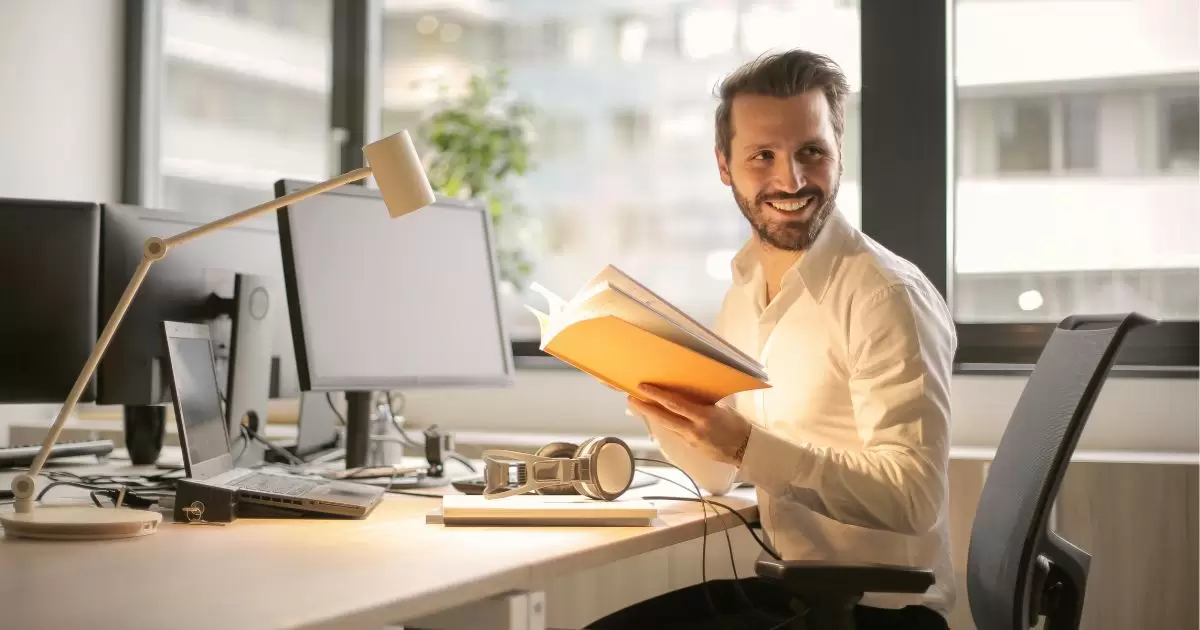 a man sitting at a desk holding a book